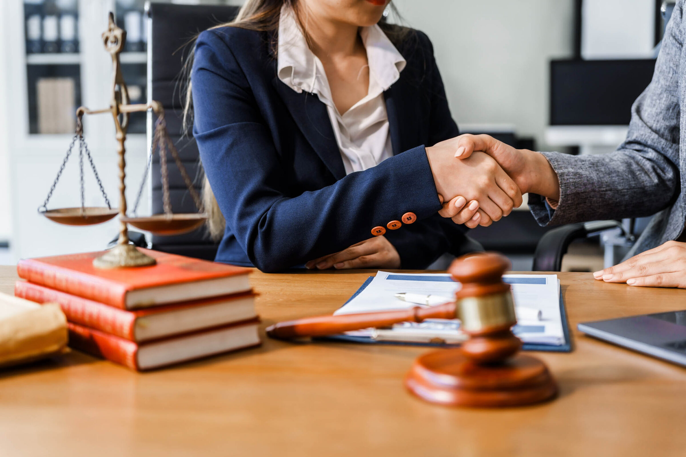 Two lawyers shake hands at wooden desk, finalizing legal agreement on car insurance dispute.