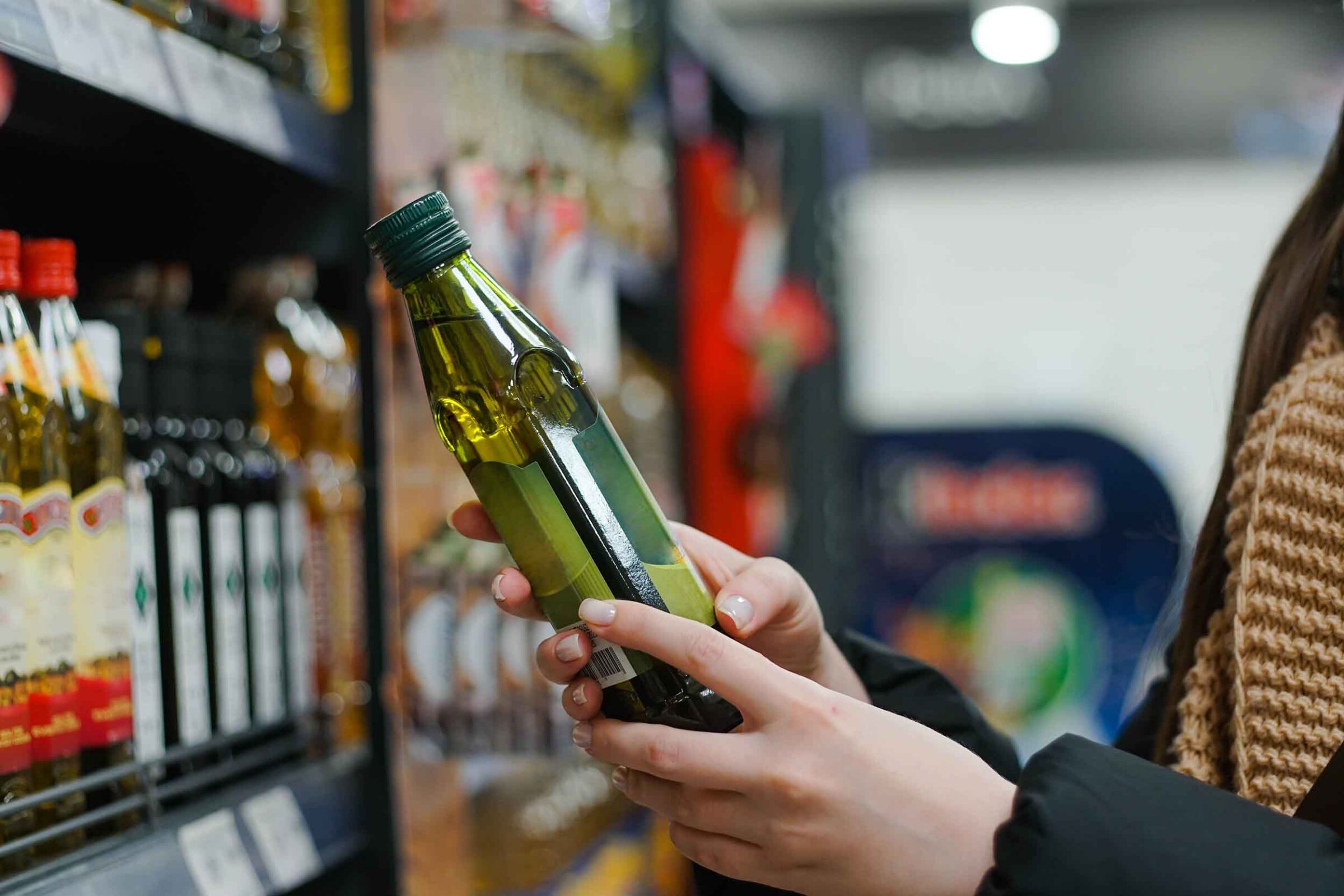 Female hand choosing natural olive oil at store.