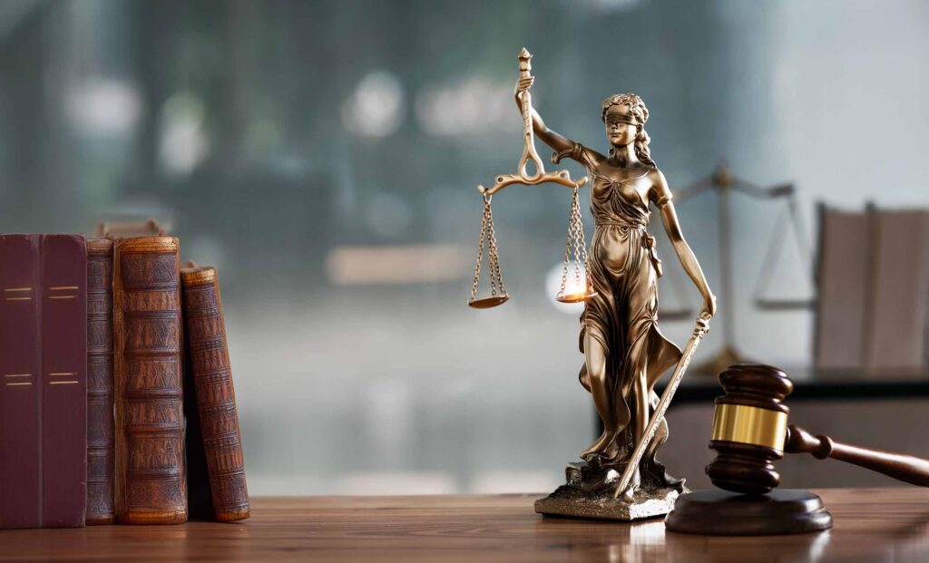 Statue of Lady Justice with scales of justice and wooden judge gavel on wooden table.