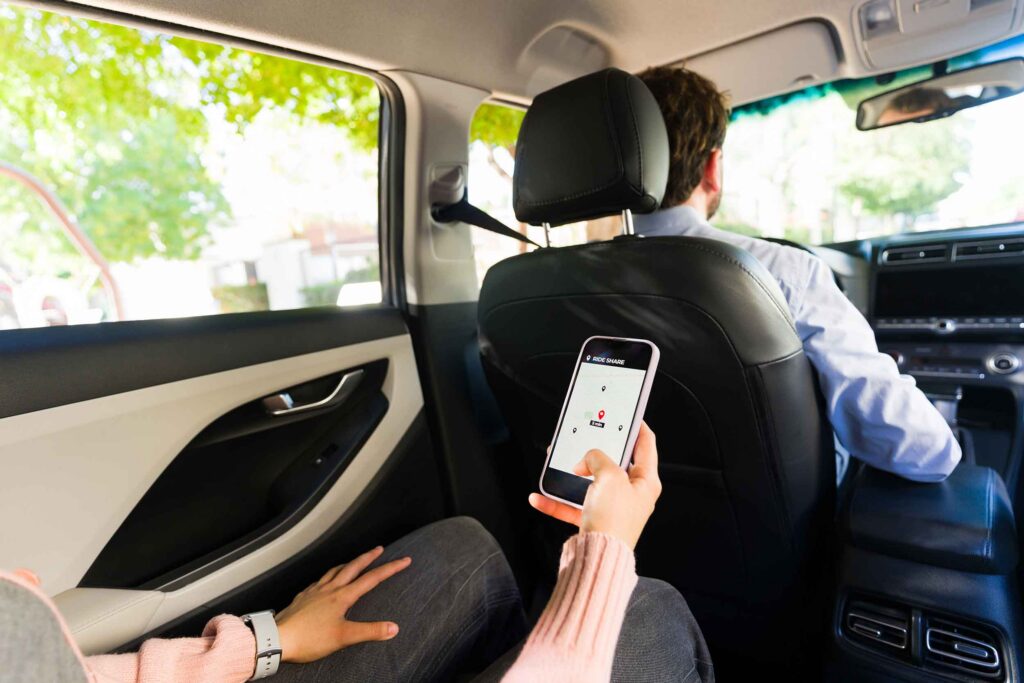 Closeup of a passenger using a smartphone with a rideshare app, tracking location and navigation while traveling in a car